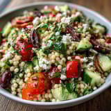 A close-up of Mediterranean Pearl Couscous topped with crumbled feta, kalamata olives, and fresh parsley, perfect for easy summer lunches.