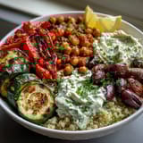 Roasted vegetables, chickpeas, and Kalamata olives mound over quinoa in a hearty Mediterranean Buddha bowl served with tangy hummus.