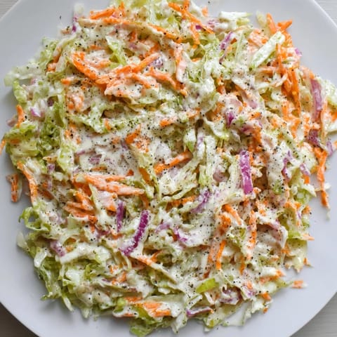 Chilled Coleslaw in a clear glass bowl showing shredded green cabbage, grated carrots, and a creamy dressing, perfect for a picnic side.