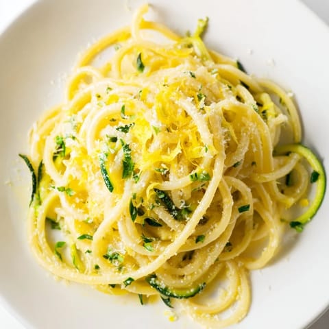 Bright yellow lemon zest and fresh parsley garnish a bowl of Lemon Zucchini Pasta, with tender green zucchini noodles and golden pasta strands twirled in a light, buttery sauce.