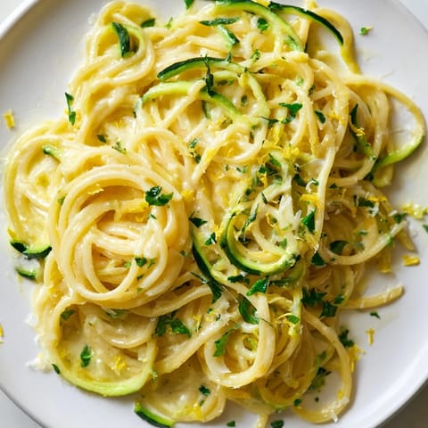 A close-up view of Lemon Zucchini Pasta shows spiralized zucchini ribbons mixed with al dente spaghetti, glistening with lemon butter sauce and freshly grated Parmesan.