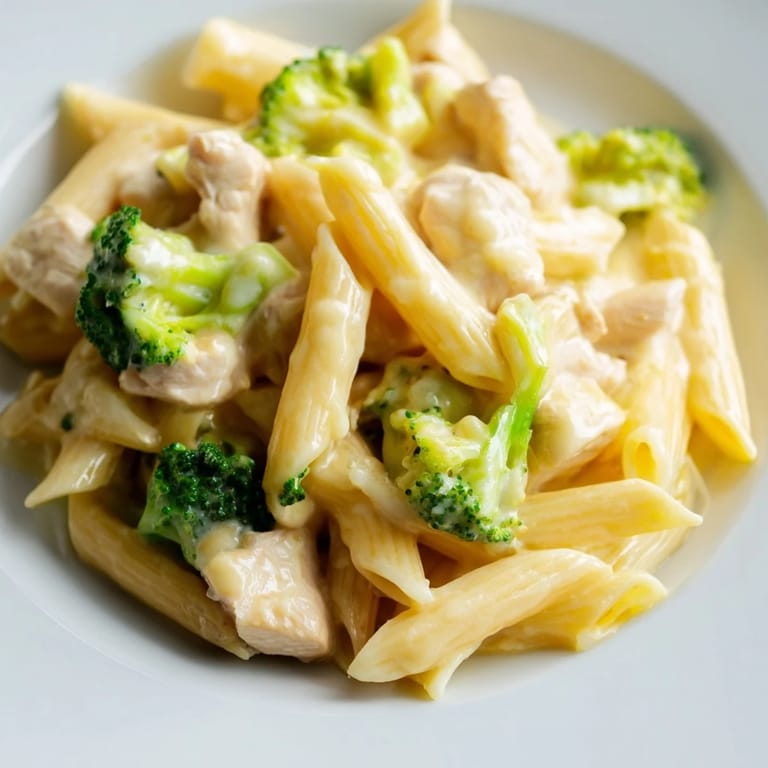 Freshly tossed Chicken Broccoli Cheddar Pasta in a white bowl, garnished with extra sharp cheddar and herbs, served alongside crisp green salad and garlic bread.