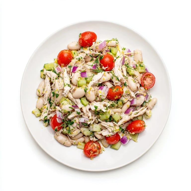 Lemony White Bean Chicken Salad in a white bowl, mixed with crisp celery, red onion, and halved cherry tomatoes on a rustic table.  