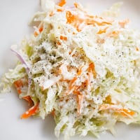 Creamy and crisp homemade Coleslaw tossed with shredded cabbage and carrots, served chilled in a white bowl next to barbecue chicken.