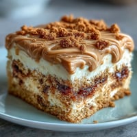 Decadent Baked Biscoff Cake with Creamy Lotus Frosting, topped with crunchy biscuit crumbles and a sweet drizzle on a rustic wooden board.