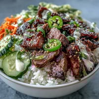 Close-up of the Korean Beef Power Bowl featuring tender sesame-ginger beef over fluffy rice with pickled carrots and cucumbers.