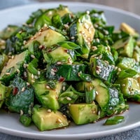 Vibrant smashed cucumber avocado salad topped with sesame seeds and green onions.